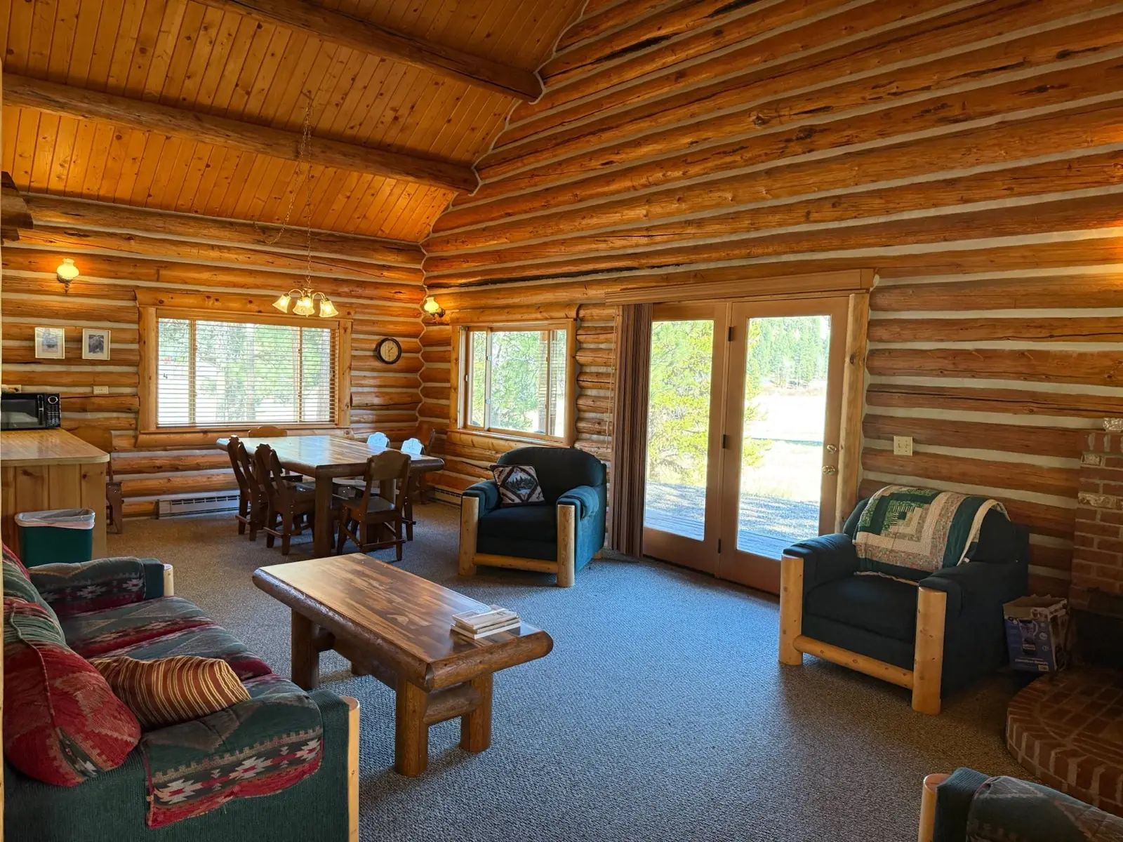 Inside the Cottonwood: a living room with log walls, a dining table and glass doors