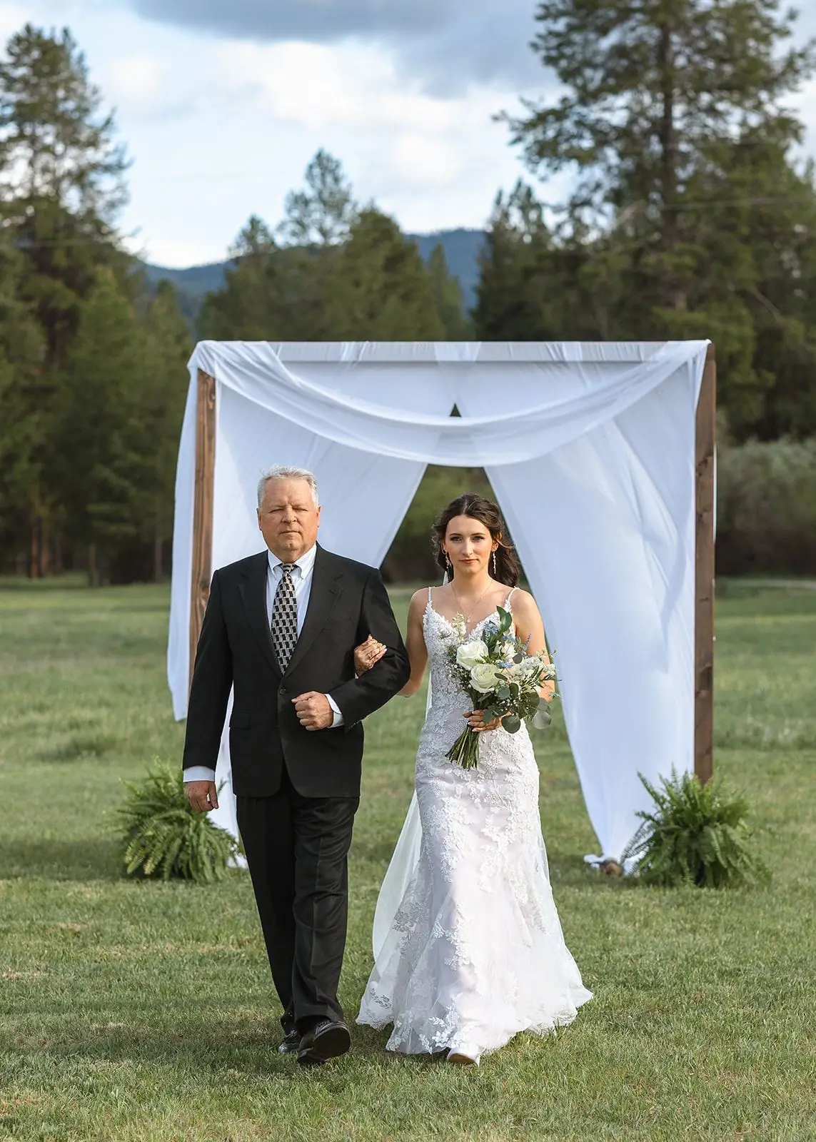 A bride walking down the aisle toward a draped ceremony arch