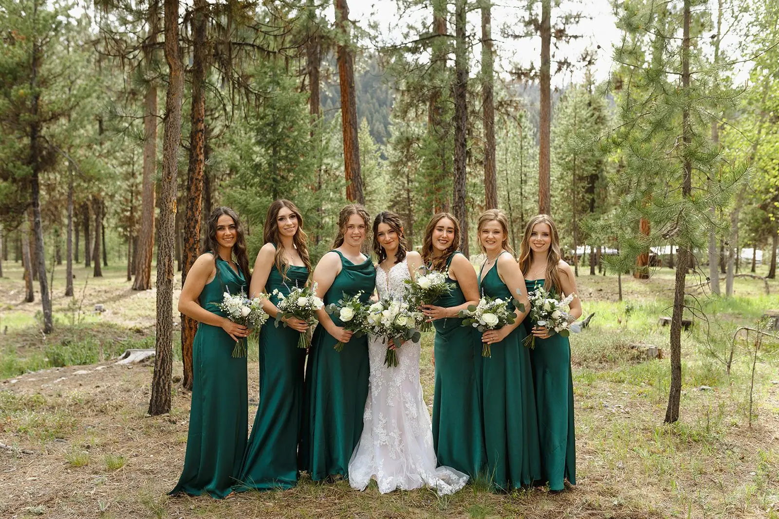 A bride with her bridesmaids in green dresses among the pines