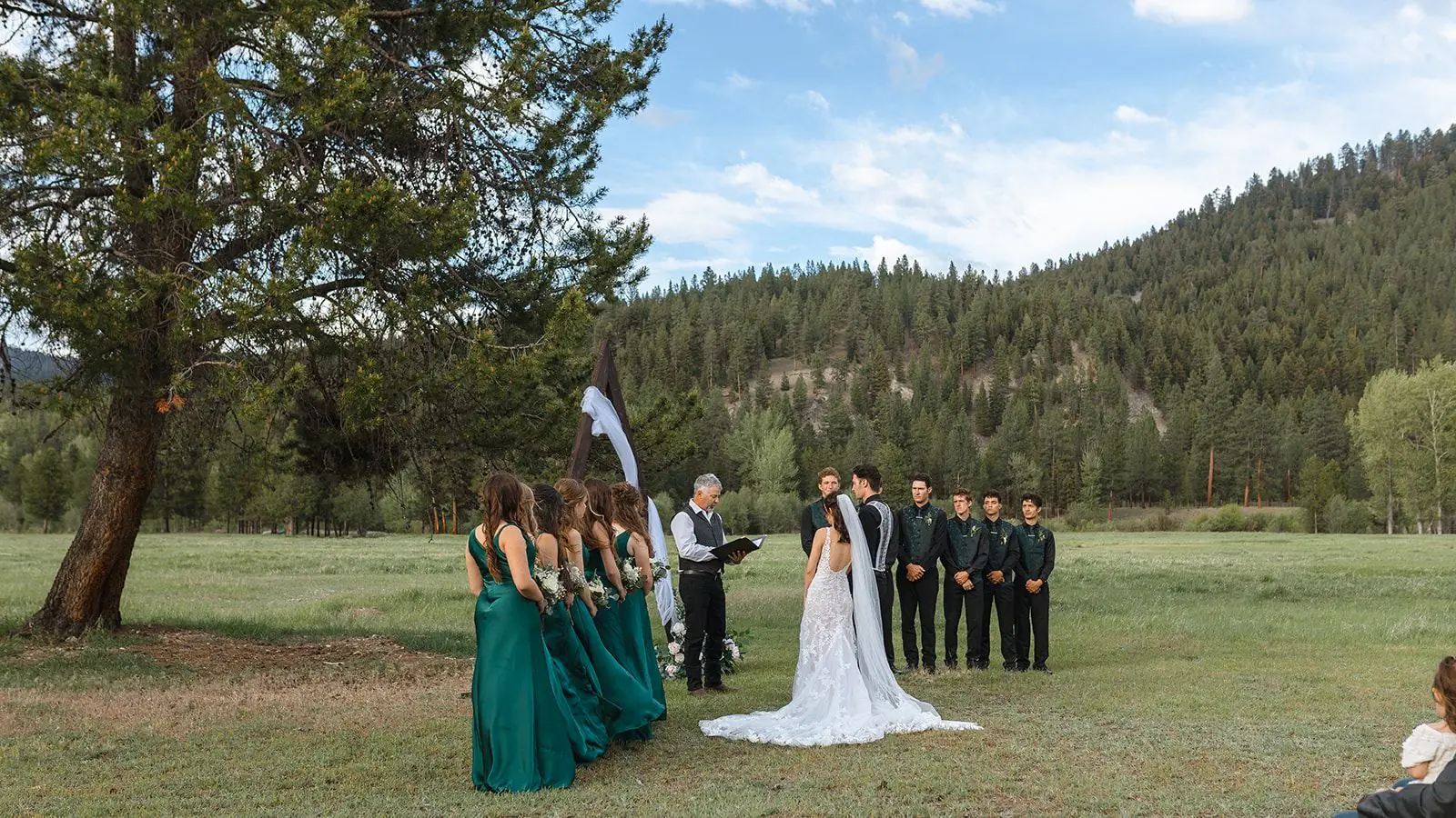 A wedding ceremony in a mountain meadow at Alta Ranch, with guests, the wedding party and forested hills behind