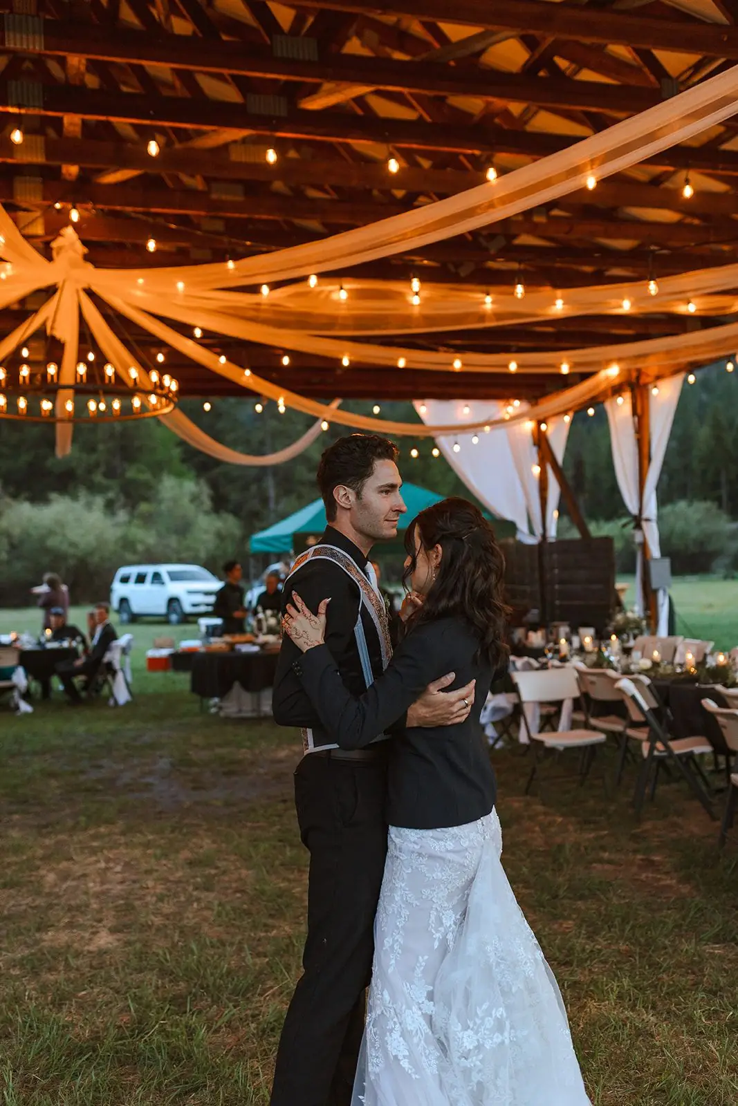 A couple sharing their first dance under string lights in the open-air hangar