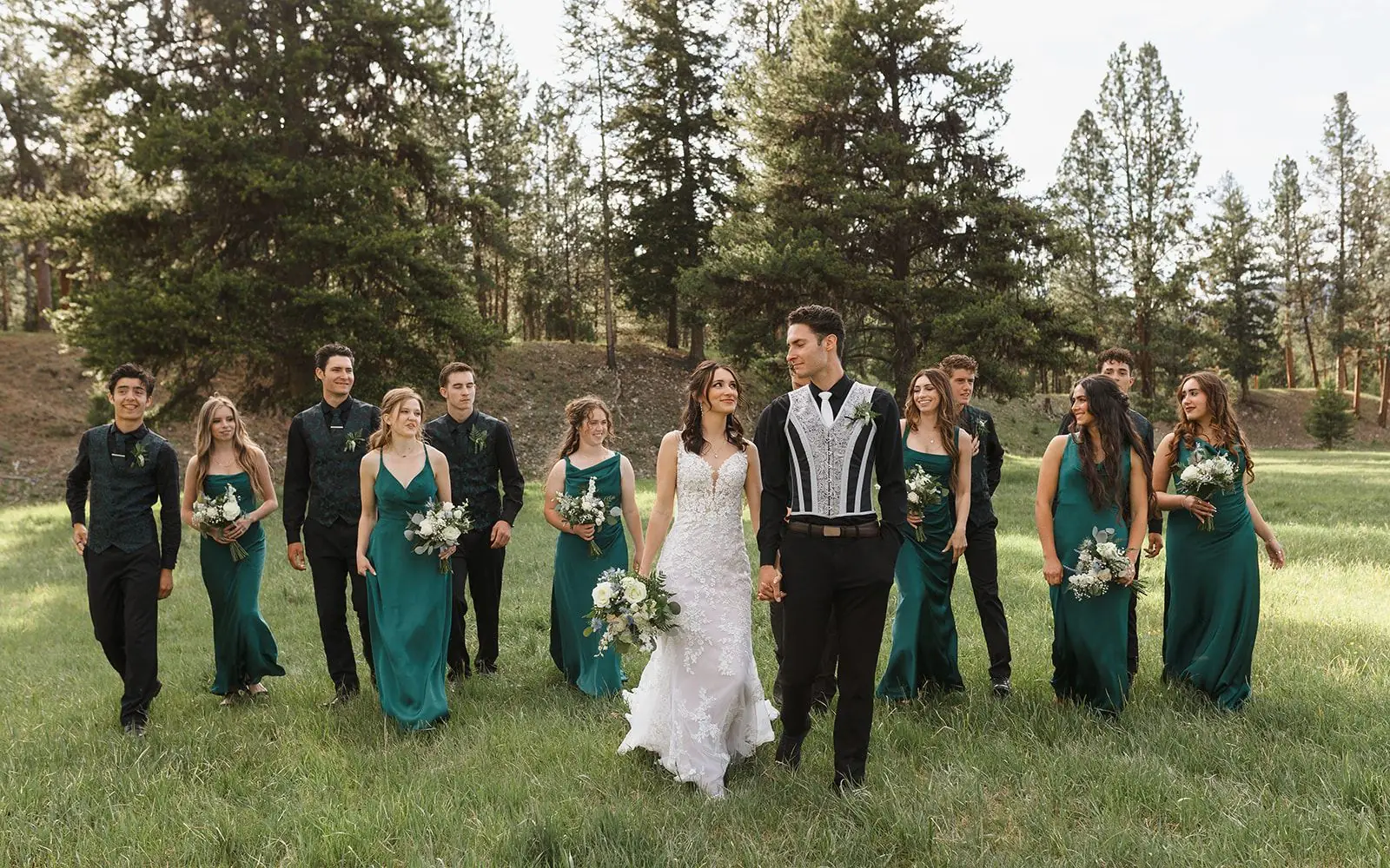 A wedding party walking through the pines in green and black